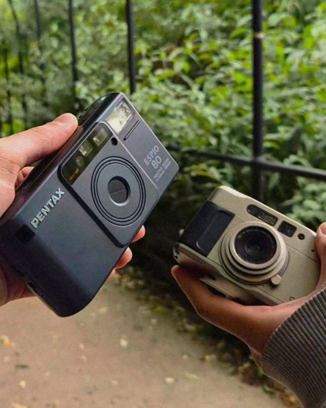 Two film cameras being held in a green outdoor park setting, highlighting 35mm film photography for a Sheffield, UK film lab that processes and develops film.