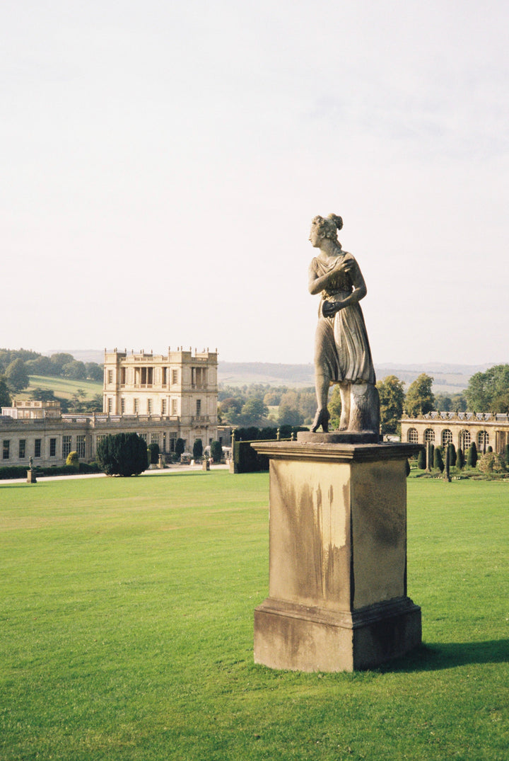 Statue on a pedestal in a park with a large building in the background, shot with Fujifilm 200 - 35mm film.