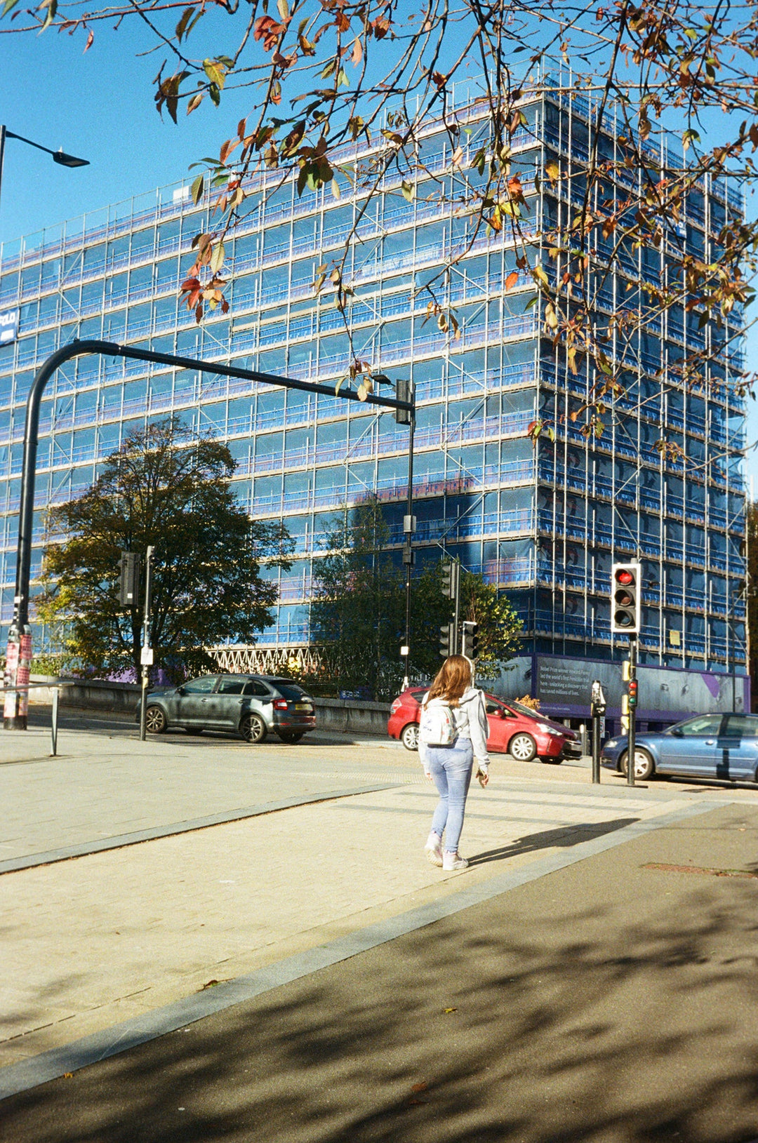 Person walking on a sidewalk with a tall building in the background, lomography color negative 400
